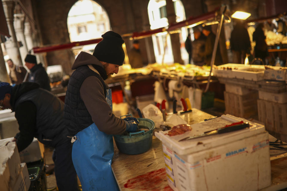 A fishmonger works in a barely empty street food market in Venice, Saturday, Feb. 29, 2020. A U.S. government advisory urging Americans to reconsider travel to Italy due to the spread of a new virus is the "final blow" to the nation's tourism industry, the head of Italy's hotel federation said Saturday. Venice, which was nearing recovery in the Carnival season following a tourist lull after record flooding in November, saw bookings drop immediately after regional officials canceled the final two days of celebrations this week, unprecedented in modern times. (AP Photo/Francisco Seco)