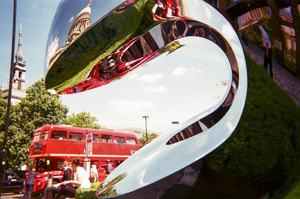 London is reflect in a statue as a red bus trundles past in the background. (Cafe Art?SWNS)