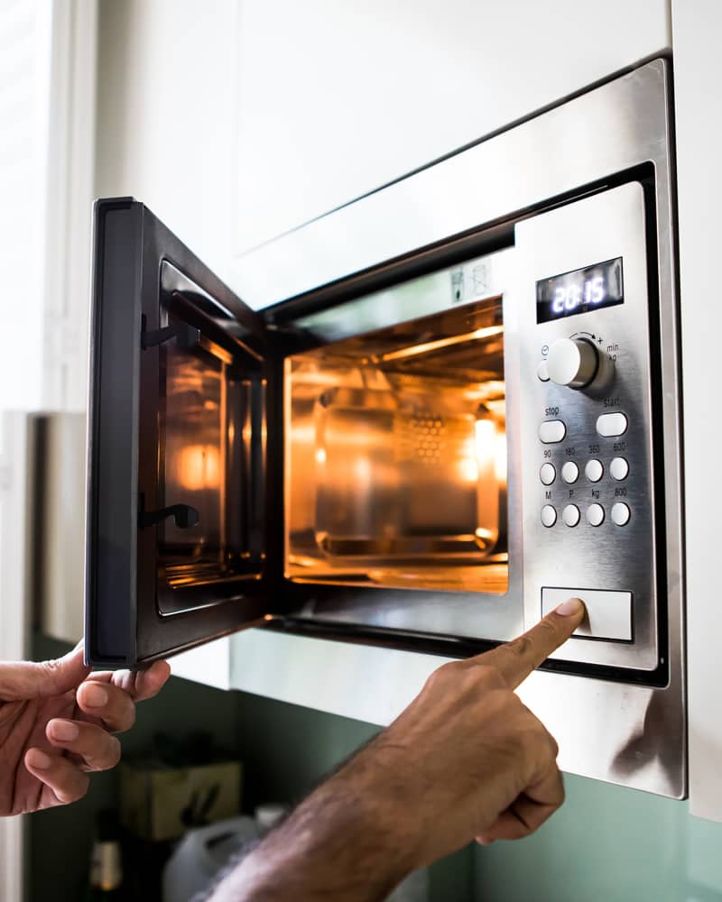 A man using a microwave oven. His finger on the opening button.