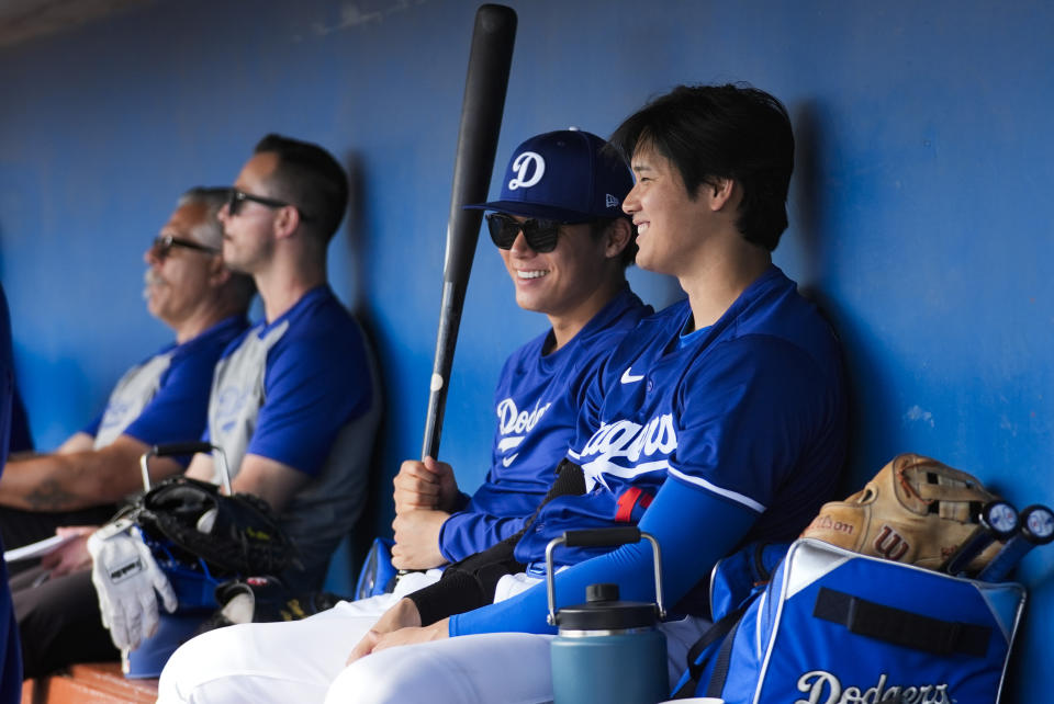 Los Angeles Dodgers relief pitcher Yoshinobu Yamamoto, center, and designated hitter Shohei Ohtani, right, sit together in the dugout during the fourth inning of a spring training baseball game against the Chicago White Sox in Phoenix, Tuesday, Feb. 27, 2024. (AP Photo/Ashley Landis)