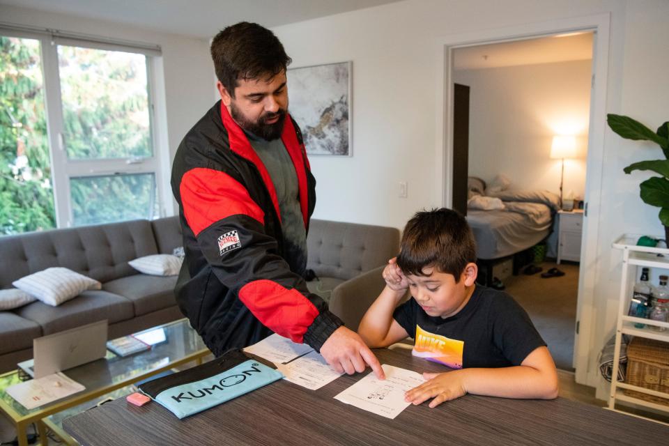 Tommy Andrade helps his son, Thaddeus, 8, with his tutoring homework at their home in Seattle. Andrade uses part of his monthly guaranteed income funds to pay for his son's tutoring.