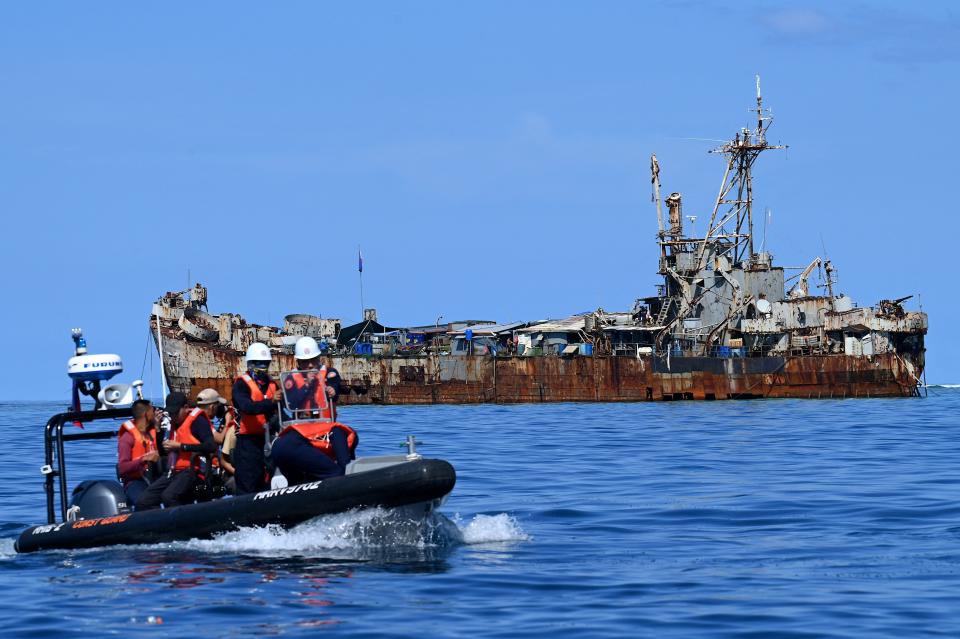 A photo of a group of people in life vests on an origin inflatable boat with the rusty BRP Sierra Madre in the background.