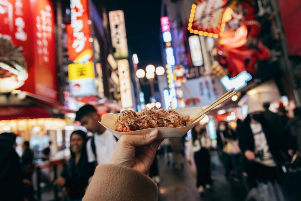 A female hand holding a plate full of takoyaki, or deep-fried octopus balls, in the city center of Osaka.