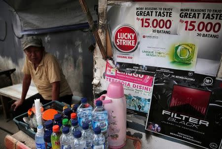 A street vendor sits near advertisements for cigarettes in Jakarta, Indonesia, May 31, 2017. Picture taken May 31, 2017. REUTERS/Beawiharta