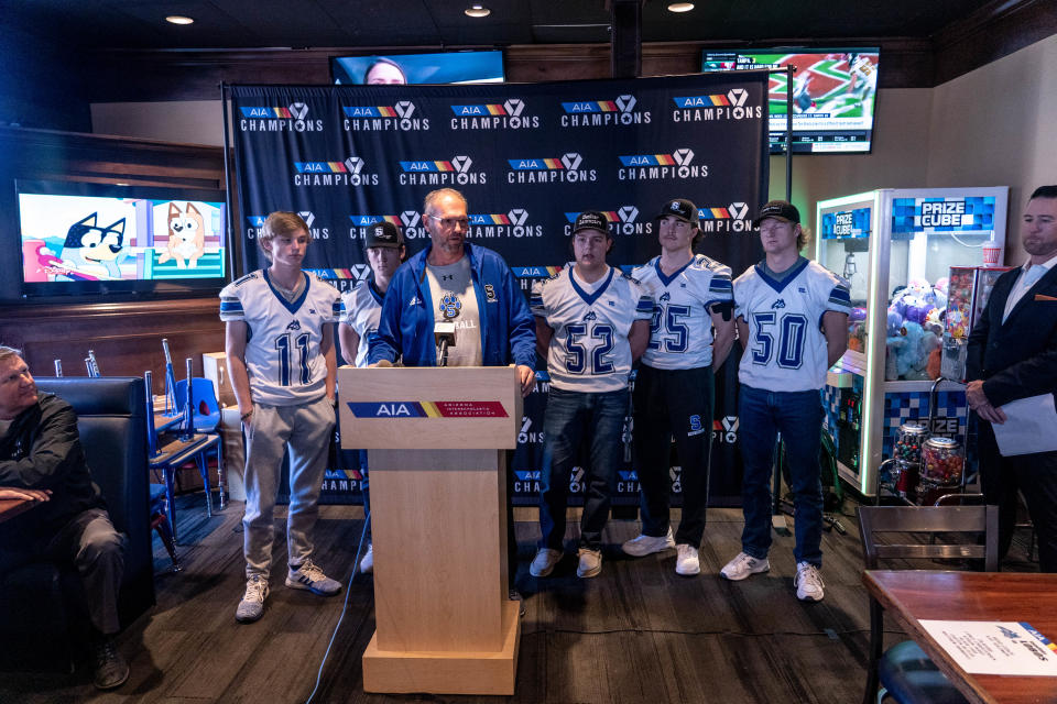 Matthew Brimhall (25) stands with coach Kay Solomon, center, and teammates from the Snowflake High School football team during the Arizona Interscholastic Association high school state championship media day at a BarroÕs Pizza in Gilbert on December 6, 2022.