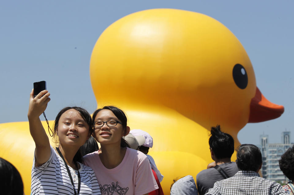 Two girls take a portrait in front of a giant yellow duck at the Glory Pier in the port of Kaohsiung, Taiwan, Thursday, Sept. 19, 2013. Putting up with the high temperatures, thousands flocked to the port of Kaohsiung, the first leg of the Taiwan tour, to see Dutch artist Florentijn Hofman's famous 18 meter (59 foot) yellow duck, a gigantic version of the iconic bathtub toy used by children around the world. (AP Photo/Wally Santana)