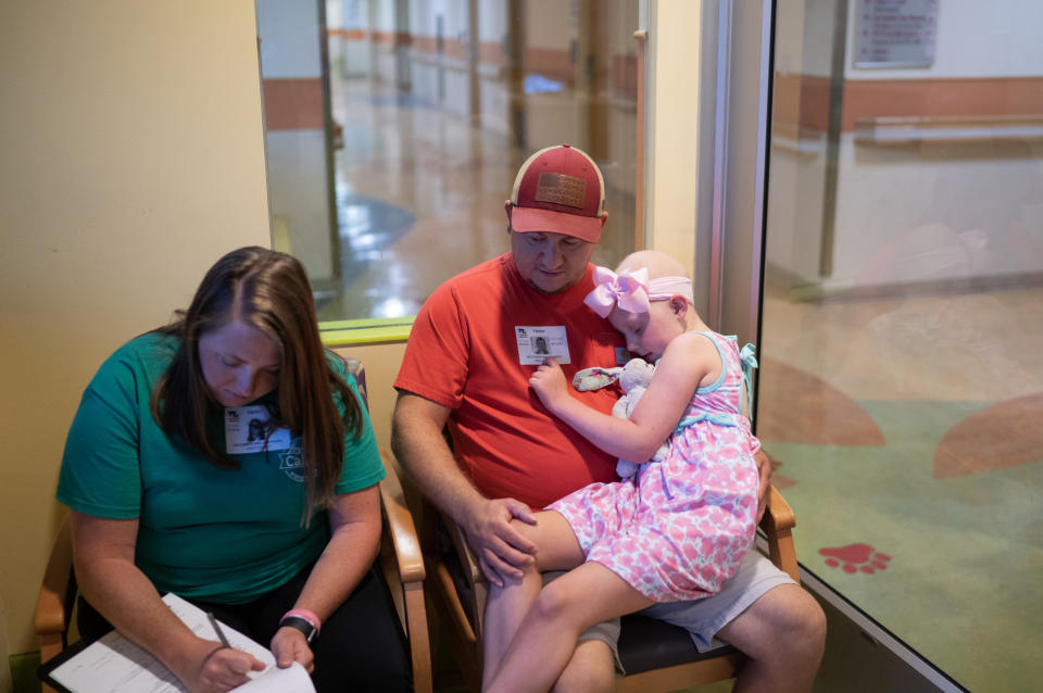 Callie Weatherford rests on her father Joey's lap while her mother, Stephanie, fills out paperwork at Children's National in D.C. The Weatherfords must drive seven hours from their home in Florence, S.C., for each visit to the hospital for Callie's treatment and checkups. (Washington Post photo by Minh Connors)