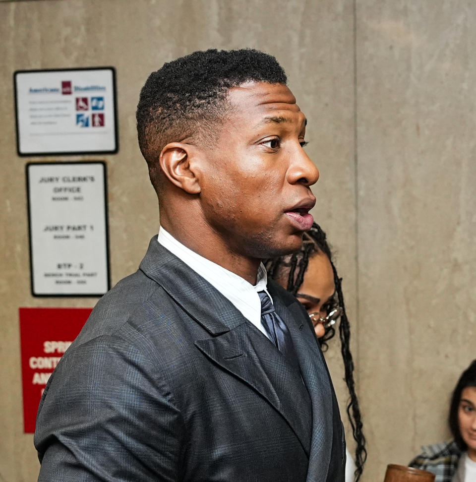 Jonathan Majors in a courtroom, wearing a suit and tie, speaking to someone off-frame