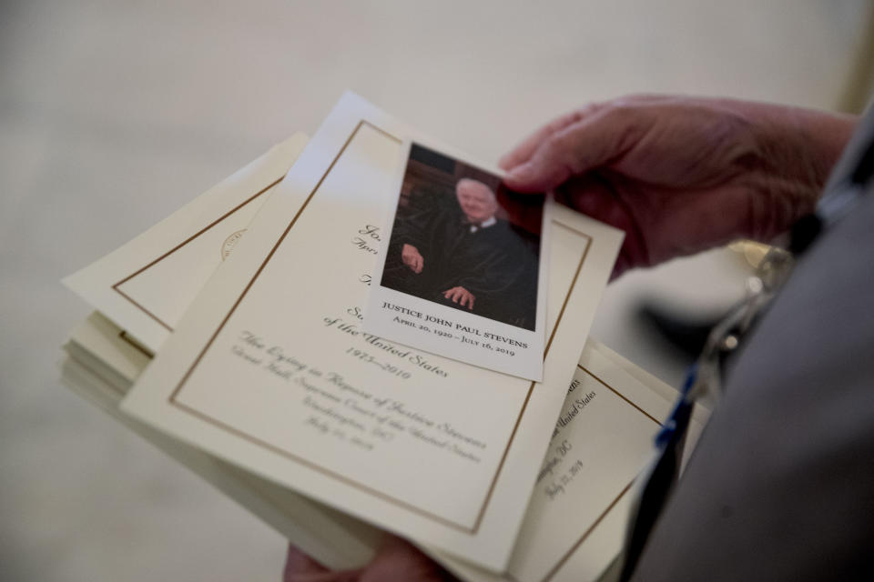 Visitors are handed a photograph and information as they pay their respects for the late Supreme Court Justice John Paul Stevens as he lies in repose in the Great Hall of the Supreme Court in Washington, Monday, July 22, 2019. (AP Photo/Andrew Harnik)