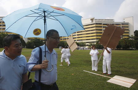 A man (2nd L) carrying a Workers' Party umbrella passes People's Action Party (PAP) supporters outside a nomination center ahead of the general elections in Singapore September 1, 2015. REUTERS/Edgar Su