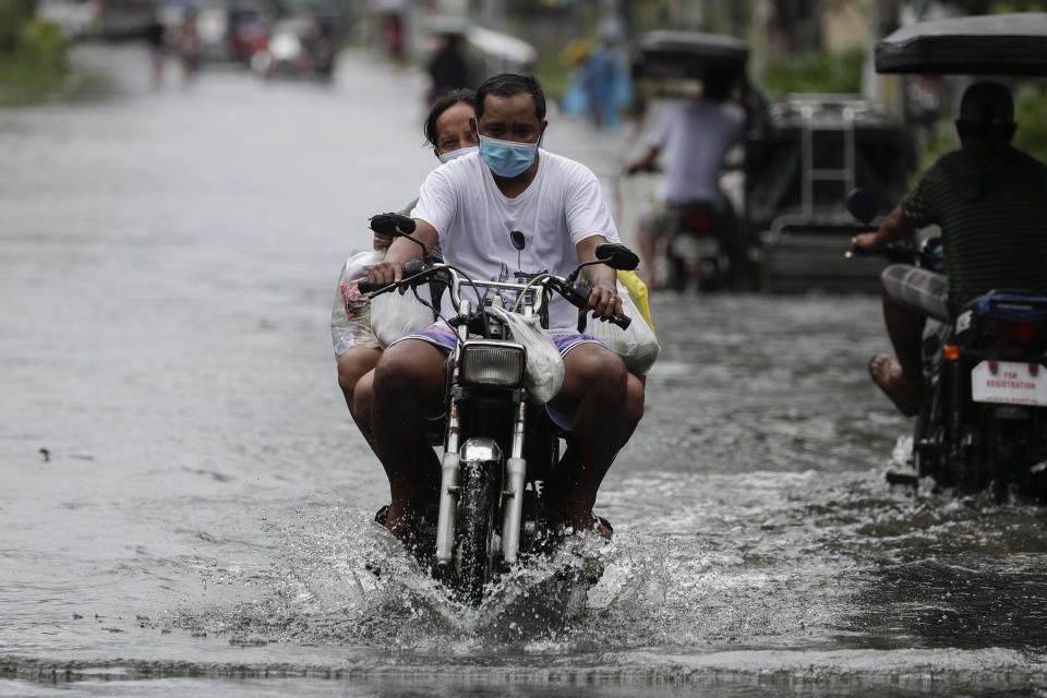 Residents on a motorcycle negotiate a flooded road due to Typhoon Molave in Pampanga province, northern Philippines, Monday, Oct. 26, 2020. A fast-moving typhoon forced thousands of villagers to flee to safety in provinces south of the Philippine capital Monday, flooding rural villages and ripping off roofs, officials said. (AP Photo/Aaron Favila)