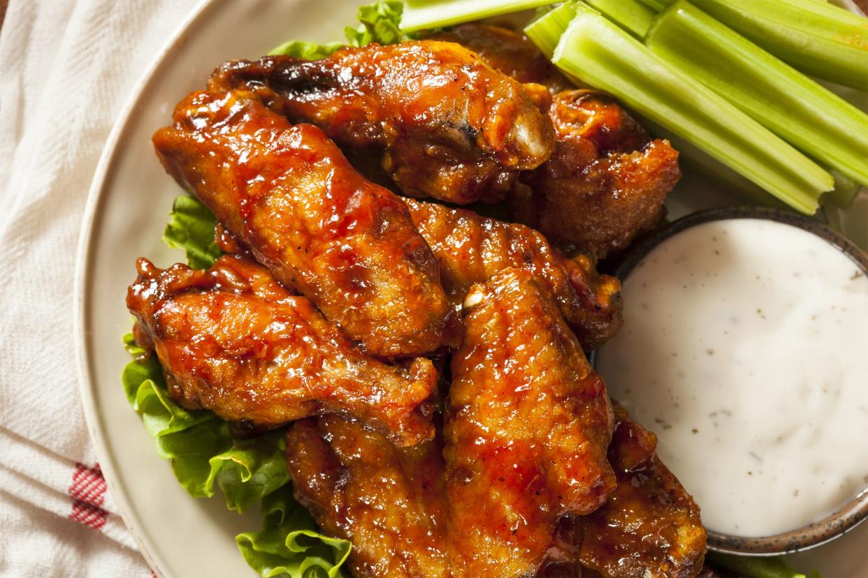 Top view of crispy baked chicken wings with celery sticks and white dipping sauce on a white plate on a white napkin