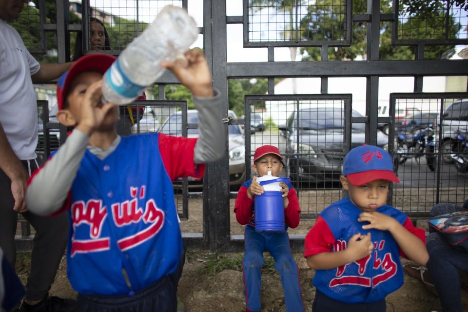 In this Aug. 12, 2019 photo, young baseball players take a water break during a practice at Las Brisas de Petare Sports Center, in Caracas, Venezuela. Sometimes, local trainers say, a player faints on the field because he hasn't had enough to eat, a sign of how nationwide shortages of food, medicine and other necessities inflict a heavy toll. (AP Photo/Ariana Cubillos)