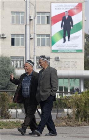 Men walk in a street, with a board displaying Tajikistan's President Imomali Rakhmon seen on a building in the background, in Dushanbe, November 1, 2013. REUTERS/Nozim Kalandarov