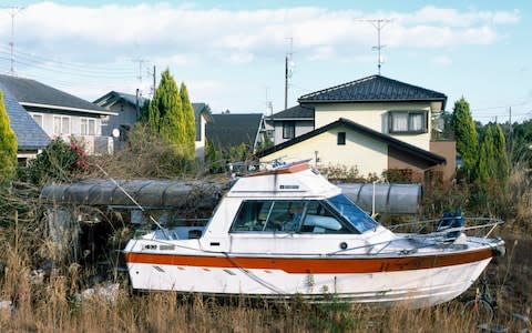 A yacht lies in the backyard of an abandoned home inside the contamination zone - Credit: Simon Townsley