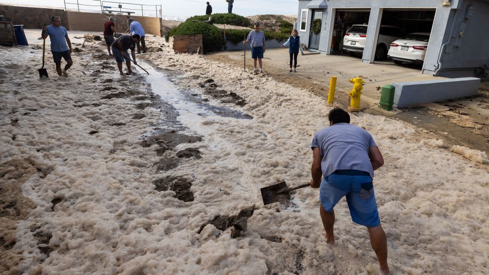 Pierpont, California, neighbors help shovel debris on Bath Lane to help water drain after a seawall and sand berm were breached by high surf on December 28. - Brian van der Brug/Los Angeles Times/Getty Images