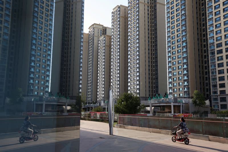 A woman rides a scooter past residential buildings at an Evergrande residential complex in Beijing