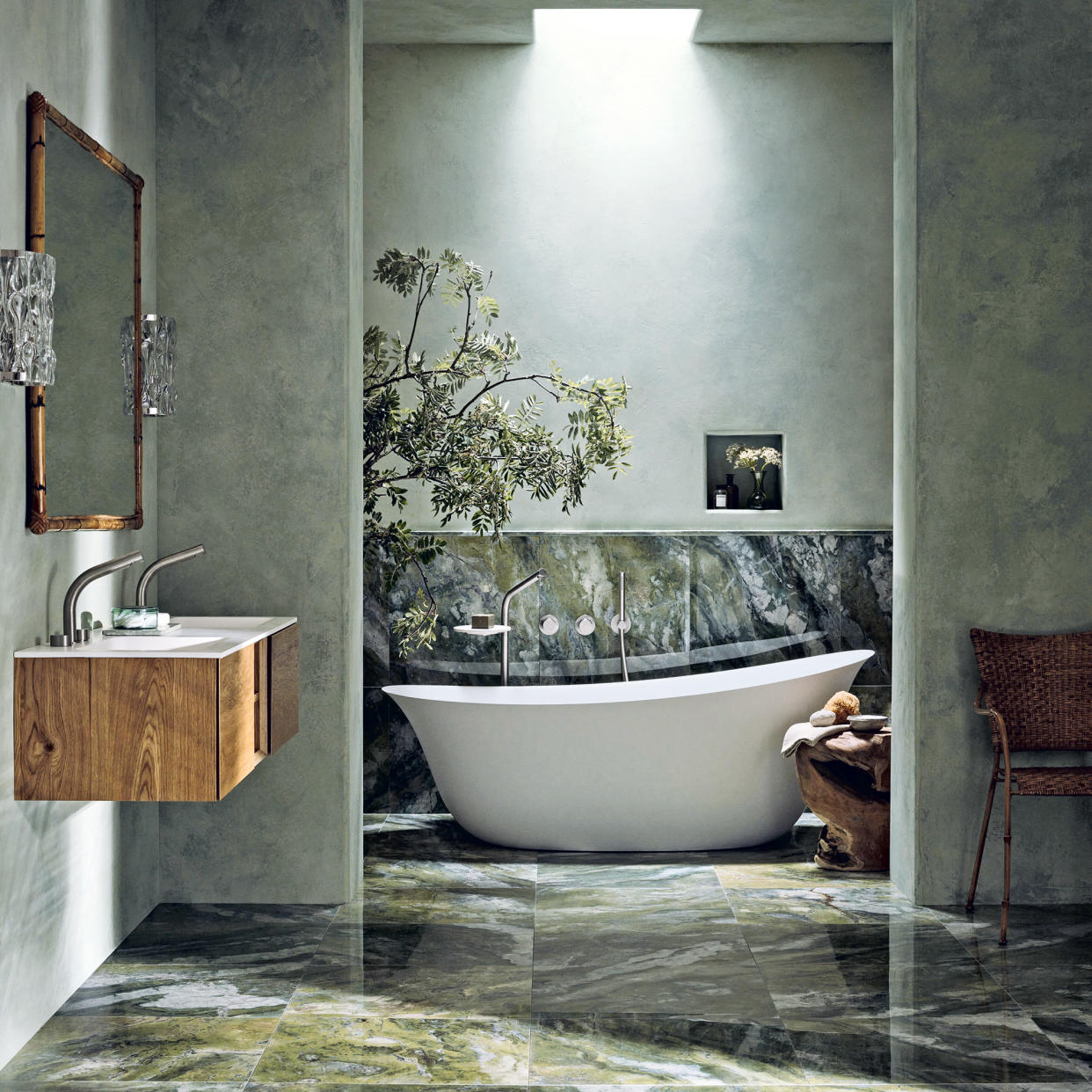  Luxe bathroom with green marble floor, wooden wall-hung vanity and modern white freestanding bath. 