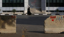 A Palestinian woman walks on a road next to barriers during a lockdown imposed following the discovery of a rise in coronavirus cases in Gaza City, Monday, Aug. 31, 2020. (AP Photo/Hatem Moussa)