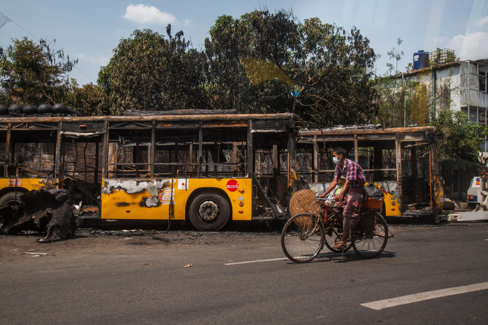 A man bikes past burnt public transport buses parked at Kyimyindaing township in Yangon, Myanmar Monday, April 12, 2021. Local news media reported that the buses got burned early Monday morning, but provided no details for the cause. (AP Photo)