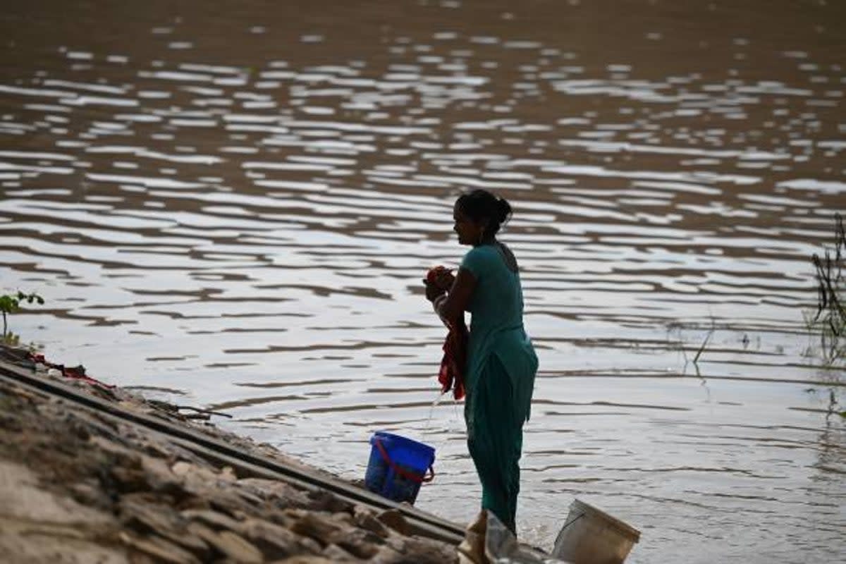 A woman does her laundry next to a flooded area near the banks of the Yamuna River  (AFP via Getty Images)