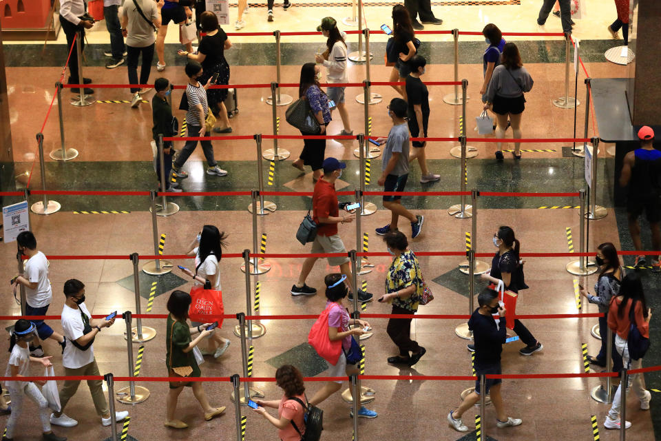 SINGAPORE - JUNE 20:  People wearing protective masks prepare their mobile phone for Safe Entry check-in as they queue to enter a shopping mall at Orchard Road on June 20, 2020 in Singapore. From June 19, Singapore started to further ease the coronavirus (COVID-19) restrictions by allowing social gatherings up to five people, re-opening of retail outlets and dining in at food and beverage outlets, subjected to safe distancing. Parks, beaches, sports amenities and public facilities in the housing estates will also reopen. However, large scale events, religious congregations, libraries, galleries and theatres will remain closed.  (Photo by Suhaimi Abdullah/Getty Images)