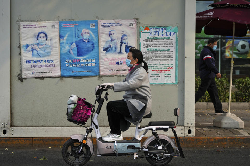 A woman rides past a coronavirus testing facility displaying posters promoting the COVID-19 vaccination in Beijing, Wednesday, Oct. 26, 2022. The Chinese city of Shanghai started administering an inhalable COVID-19 vaccine on Wednesday in what appears to be a world first. (AP Photo/Andy Wong)