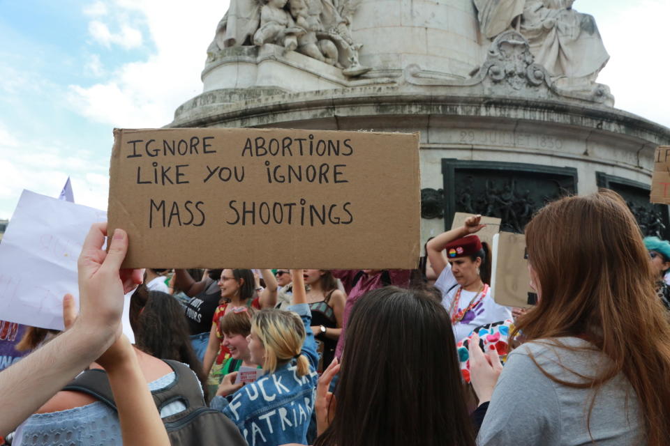 Someone holding a sign that says, "Ignore abortions like you ignore mass shootings."