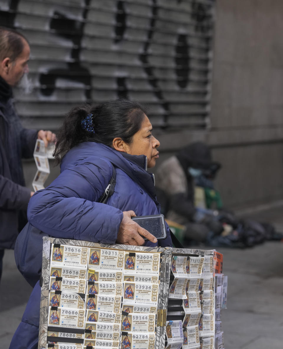 A woman carries a board of Christmas lottery tickets to sell in downtown Madrid, Spain, Wednesday, Dec. 21, 2022. People are buying last minute Christmas lottery tickets for Spain's bumper Christmas lottery draw known as El Gordo, or The Fat One, which will be held on Dec. 22. (AP Photo/Paul White)