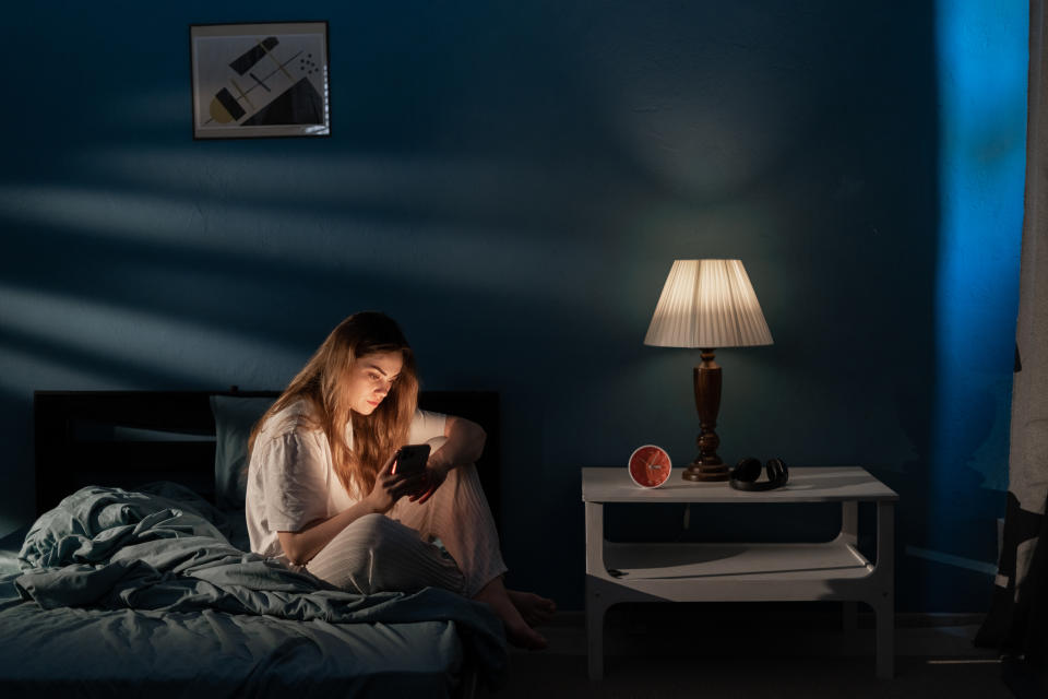 Young woman sitting on bed using mobile phone late at night, suffering from insomnia, chatting in social media network. Internet addiction concept