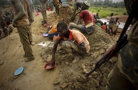 A gold prospector sits and eats close to a soldier at a gold mine near the village of Gamina, in western Ivory Coast, March 18, 2015. REUTERS/Luc Gnago