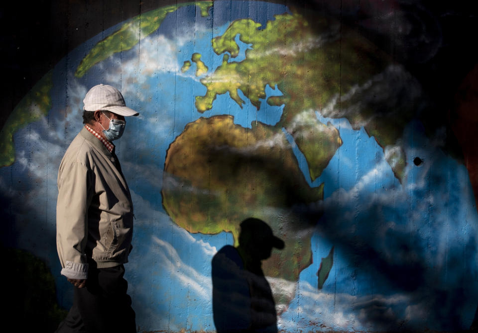 FILE - In this Monday, Sept. 28, 2020 file photo, a man wearing a mask walks past graffiti depicting a globe at Orcasitas neighborhood in Madrid, Spain. Public health experts say 1 million worldwide deaths are among reasons to be concerned, if not fearful, of the coronavirus and take everyday precautions despite much rosier advice from the still recovering Donald Trump. (AP Photo/Manu Fernandez)