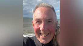 A selfie of Phil Edwards with grey hair and a black top smiling at the camera in front of the sea