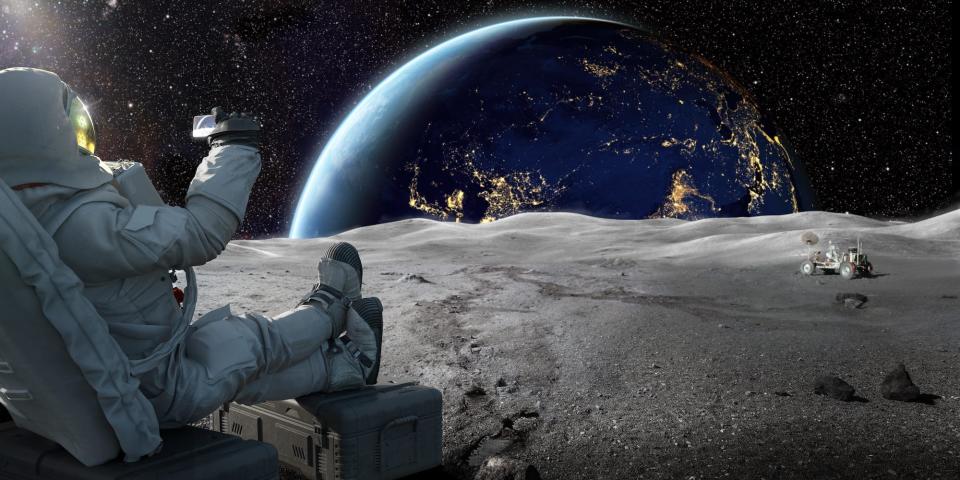 An artist's impression shows an astronaut sitting back while taking a picture of the Earth rising behind the surface of the moon with a smartphone.