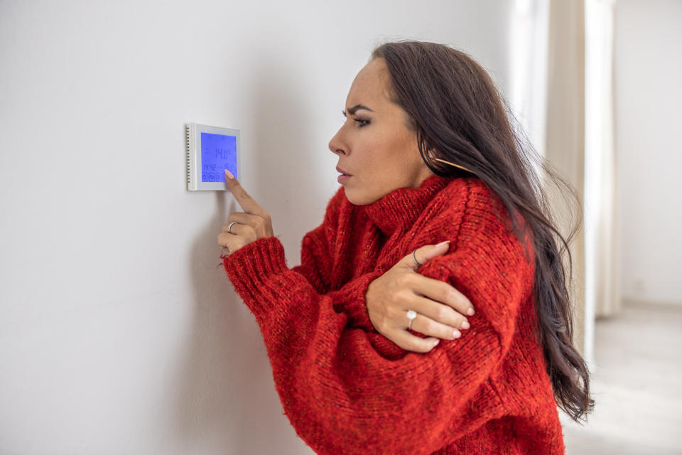 A woman who is cold turning on her thermostat