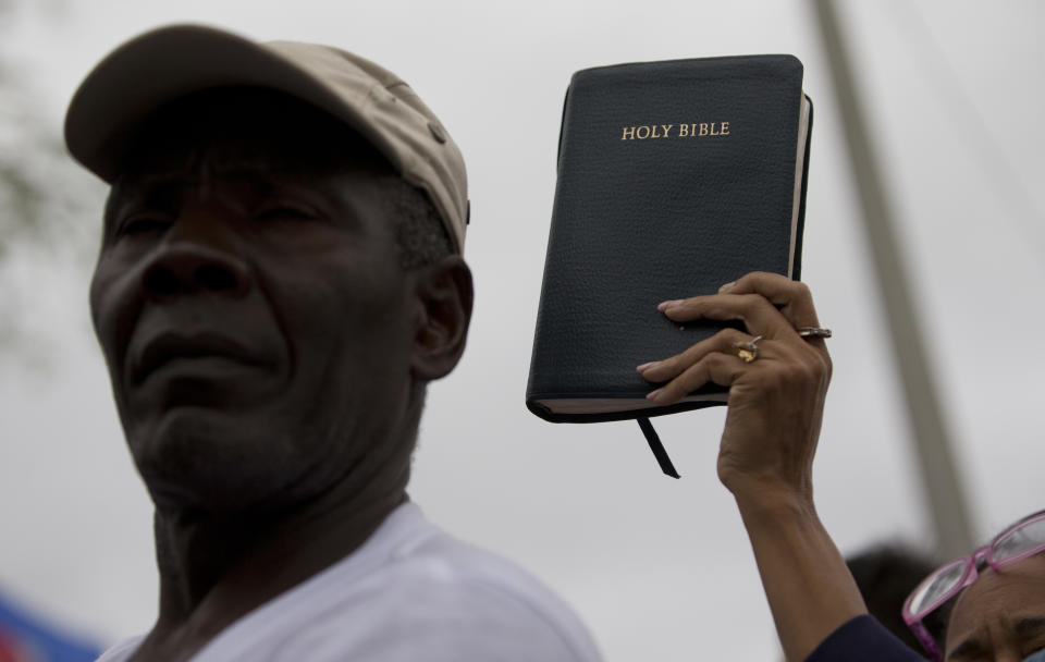 <p>Pastor Marie Belizaire, lower right, holds a bible as she listens to a news conference condemning President Trump’s recent remarks denigrating Haiti, before a march to commemorate the eighth anniversary of the Haitian earthquake, Friday, Jan. 12, 2018, in Miami, Fla. (Photo: Wilfredo Lee/AP) </p>