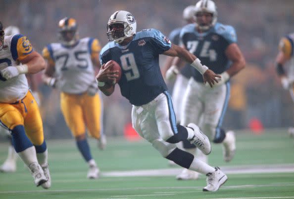 steve mcnair runs with the football as players from the opposing team chase him, all the men wear football uniforms and helmets