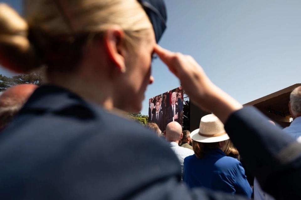 Madison Marsh salutes with Joe Biden on a large videoscreen in the background