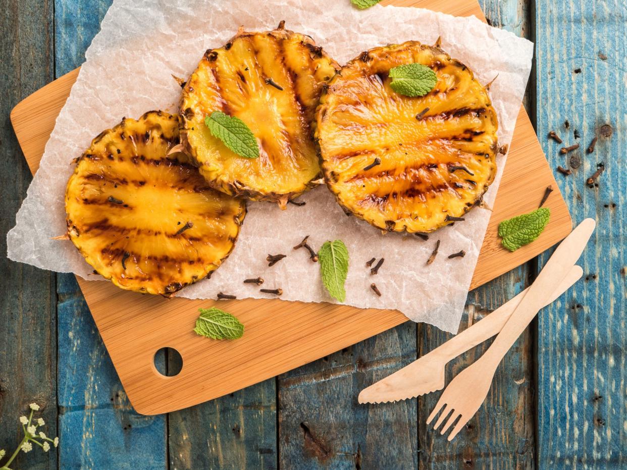 three slices of grilled pineapple on a wooden cutting board garnished with mint leaves