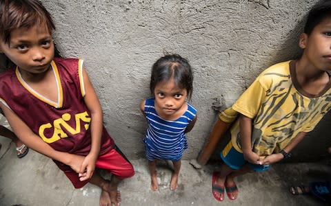 Ashlie Arangues, who is stunted, stands next to two children of a similar age – a stark illustration of how malnutrition has affected her development - Credit: Simon Townsley