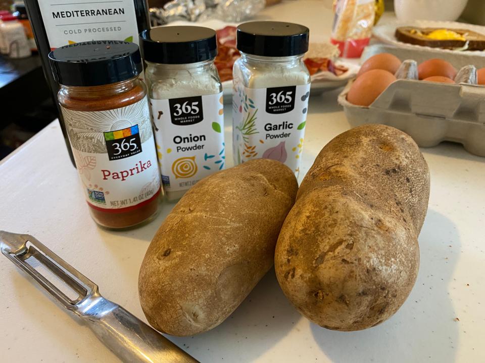 potatoes, peeler, and seasoning on cutting board