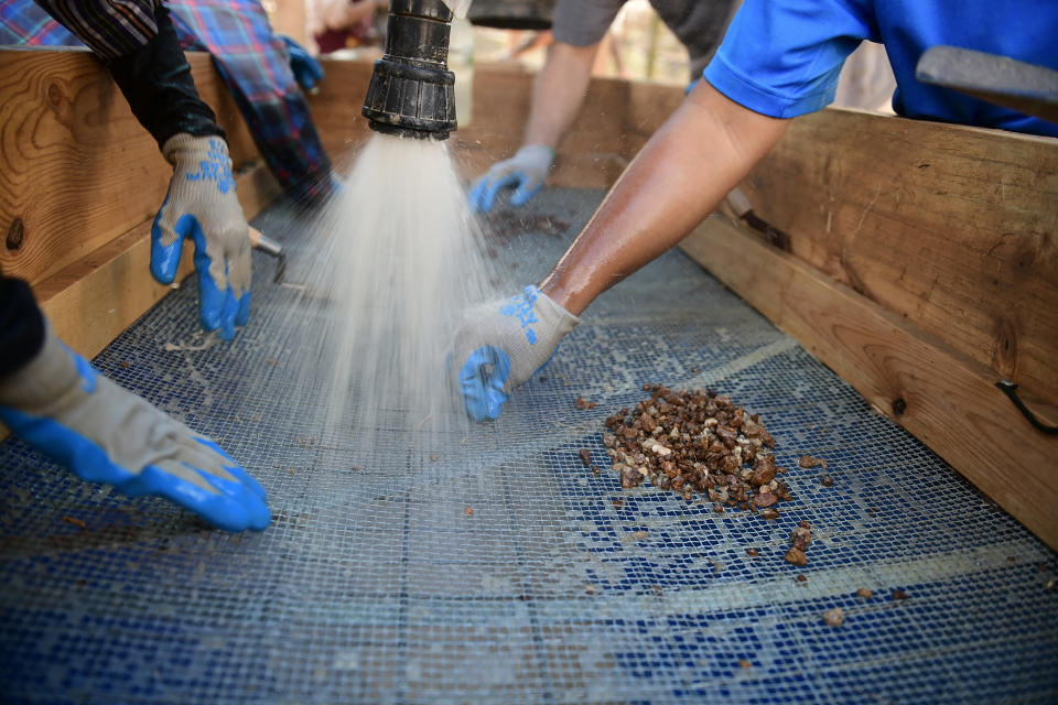 Team members assigned to the Defense POW/MIA Accounting Agency (DPAA), sifts through dirt on the wet-screen station alongside local workers during an excavation operation in in Lampang province, northern Thailand, March 2, 2022. Possible human remains were found at a crash site in a rice field in northern Thailand by the Defense POW/MIA Accounting Agency and were sent to Hawaii where they will be tested to see if they belong to a U.S. pilot who went missing in 1944. (U.S. Army Sgt. 1st Class Michael O'Neal/Defense POW/MIA Accounting Agency via AP)