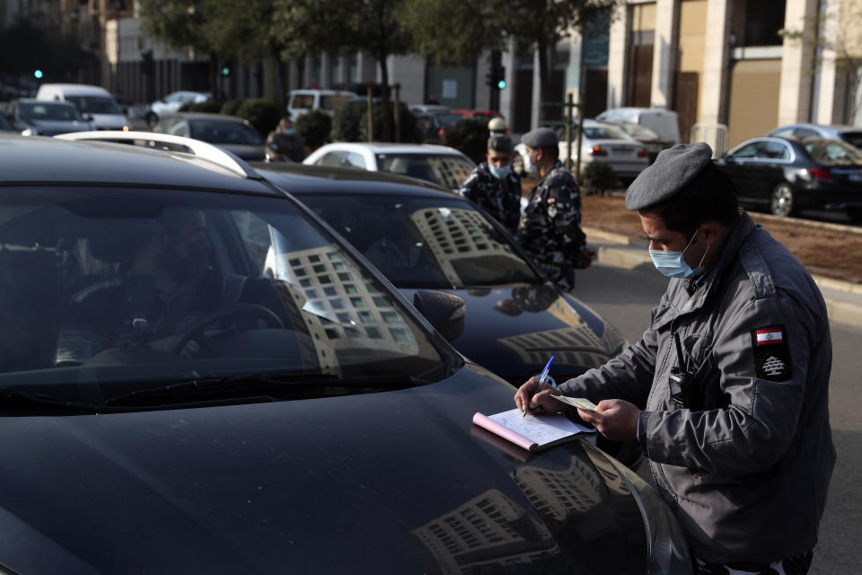 A police officer issues fines on vehicles that violate the odd and even license plate rule on alternating days as the country began a three-week lockdown to limit the spread of coronavirus amid a post-holiday surge in the past 10 days in Beirut, Lebanon, Thursday, Jan. 7, 2021. (AP Photo/Bilal Hussein)