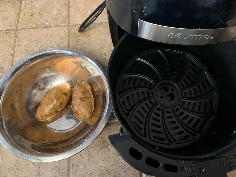 Two potatoes in a metal bowl beside an open air fryer