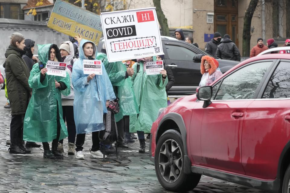 Demonstrators hold posters reading "Say No to genocide" as they try to block a street during an anti-vaccination protest in Kyiv, Ukraine, Wednesday, Nov. 3, 2021. In a bid to stem contagion, Ukrainian authorities have required teachers, government employees and other workers to get fully vaccinated by Nov. 8 or face having their salary payments suspended. In addition, proof of vaccination or a negative test is now required to board planes, trains and long-distance buses. (AP Photo/Efrem Lukatsky)