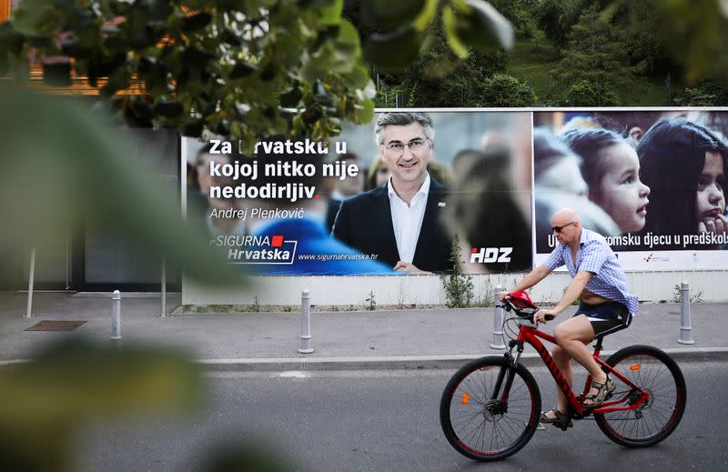 A man rides a bike past a banner advertising the campaign of Croatian Prime Minister and the leader of the centre-right Croatian Democratic Union (HDZ) Andrej Plenkovic in Zagreb