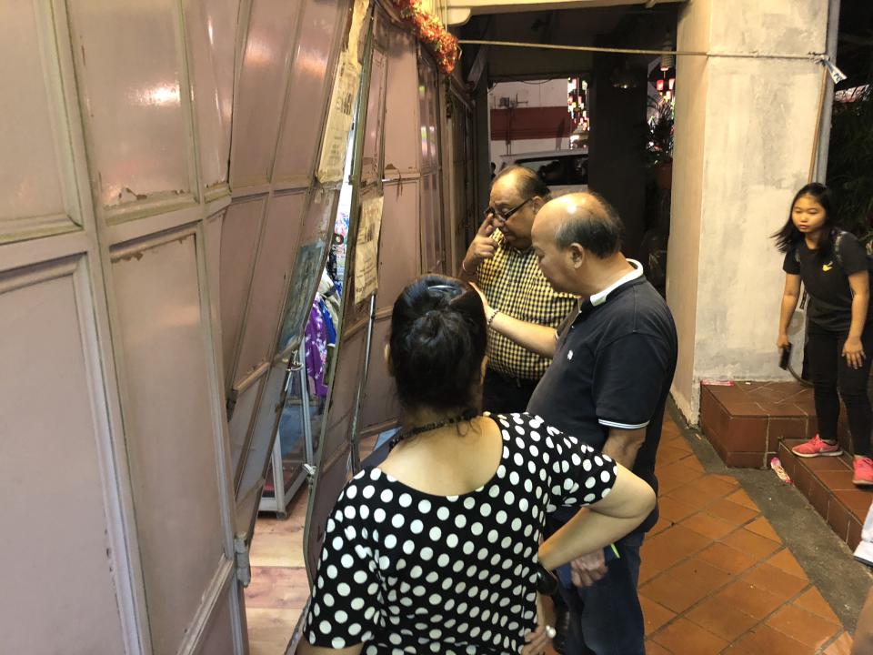 Shop owner Harry Ramchand (in yellow checked shirt), assessing damage to his shop door after the accident. (PHOTO: Teng Yong Ping/Yahoo News Singapore)