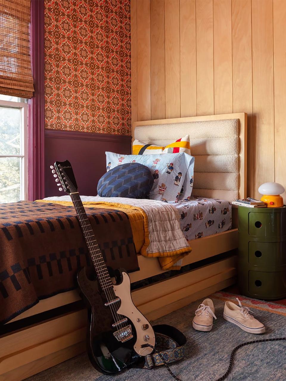 Teen bedroom with wood paneled wall and burgundy patterned wallpaper. 