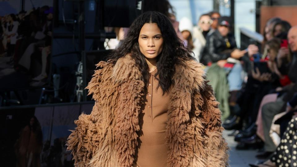 A model walks the runway during the Stella McCartney Womenswear Fall/Winter 2024-2025 show wearing a ribbed brown body suit and oversized fluffy coat