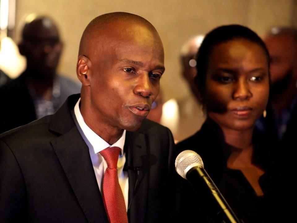 Jovenel Moise speaks into a microphone while Martine Moise, his wife, looks on.